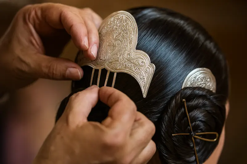 Primer plano de las manos de un profesional colocando la peineta trasera en un moño de fallera.